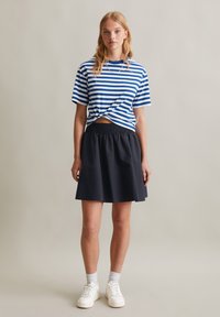 Gestreepte blauw-witte katoen t-shirt met een geknoopte detail aan de voorkant, gecombineerd met een zwarte A-lijn rok met elastische taille en witte sneakers.