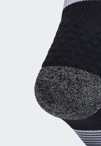 Chaussette noire avec talon et pointe gris, présentant une texture côtelée et des rayures horizontales près du haut. Le matériau semble tricoté et extensible.