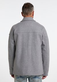 Grijze wolmix jas met gestructureerde schoudernaden, notcollar en rugventilatie, gecombineerd met lichtblauwe jeans met subtiele stiksels.