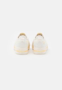 Sneakers bianchi in tela con accenti gialli, suola piatta in gomma, punta rotonda e dettagli cuciti. Presenta un tassello sul retro per il trasporto e il marchio sul tallone.