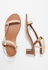 Beige lädersandaler med tunna remmar, en brun sula och en liten klack. Designen har en minimalistisk stil med en slät yta.