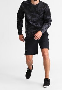 Maglietta a maniche lunghe in camouflage nero abbinata a pantaloni corti sportivi neri. L'outfit presenta tessuto traspirante ed è completato da scarpe da ginnastica nere.