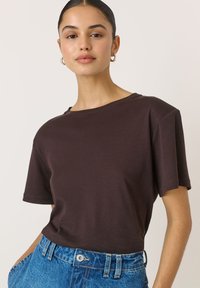 Hnědé tričko s krátkým rukávem, kulat�ým výstřihem a volným střihem, vyrobené z měkké tkaniny. Texturovaný, čistý design spojený s modrými džínami s vysokým pasem.