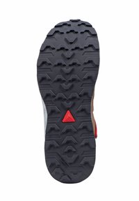 Suola della scarpa con un robusto design in gomma nera, caratterizzata da motivi di battistrada testurizzati, un accento centrale a forma di triangolo rosso e una forma aerodinamica.