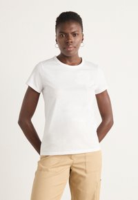 White cotton t-shirt with short sleeves, round neckline, and subtle floral design in the front. Worn with beige pants.