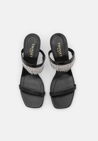 Svarta sandaler med platta sulor. Har en bred rem prydd med silverfärgade rhinestones och två smala remmar över foten.