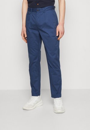 Marineblaue Baumwollhosen mit lässigem Schnitt, ausgestattet mit einem Knopfverschluss und Gürtelschlaufen, kombiniert mit weißen Sneakers.