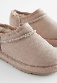 Des chaussures à enfiler en suede rose avec une doublure en fourrure douce, présentant un accent cousu le long du bord supérieur et une semelle en caoutchouc texturé.
