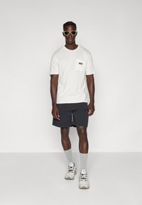 White short-sleeve t-shirt with a chest pocket, paired with black shorts, gray socks, and light athletic shoes. Accessories include sunglasses.