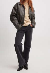 Veste bomber en cuir noir, pull en tricot beige, jean noir à coupe droite et chaussures noires à bout pointu. Textures lisses et coupe classique.