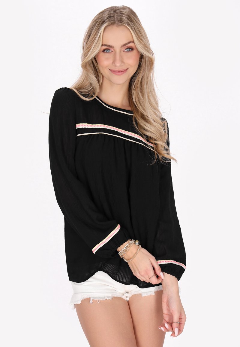 Top nero a maniche lunghe in tessuto testurizzato, con accenti a righe rosa e crema sul colletto e sui polsini, abbinato a pantaloni corti bianchi.
