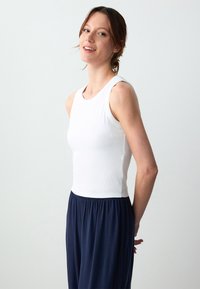 Top aderente bianco con texture a costine e design senza maniche, abbinato a pantaloni larghi in blu navy con vita elastica.