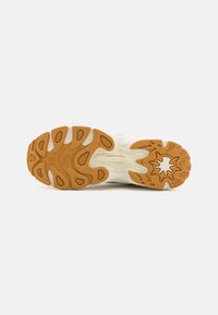 White sneaker sole with a textured rubber design and a distinctive brown traction pattern. Features a rounded shape and prominent grooves.
