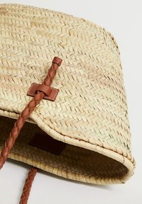 Geweven strooien tas met een natuurlijke kleur, textuur en een bruine gevlochten leren sluiting met een rechthoekig accent. Ontwerp met open bovenkant.