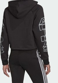 Svart kort hoodie med huva, med vit logotext längs ärmarna och ribbade muddar. Kombinerad med svarta byxor och tre vita ränder.