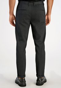 Tumehallid kohandatud püksid, millel on sile tekstuur, kaks tagataskut ja rullitud mansetid, millele on lisatud mustad kingad.