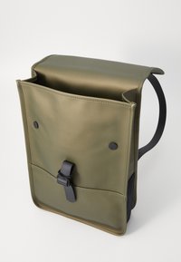Sac à dos vert olive, finition mate, avec un rabat, une poche avant et des accessoires noirs. Il est équipé de bretelles réglables et de fermetures à bouton.