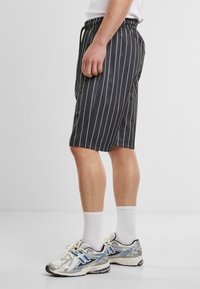Shorts noirs avec des rayures blanches verticales, tissu à finition lisse, ceinture élastique et se terminent juste au-dessus du genou.