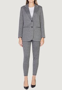 Blazer a spina di pesce grigio con due bottoni e tasche a soffietto, abbinato a pantaloni aderenti coordinati; entrambi sono realizzati in tessuto testurizzato.
