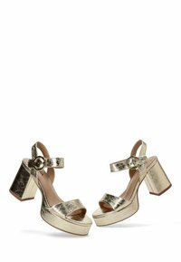 Zapatos de tacón plataforma metálicos dorados con anchos tacones rectangulares, diseño de punta abierta, tira en el tobillo con hebilla redonda y textura de cuero agrietado.