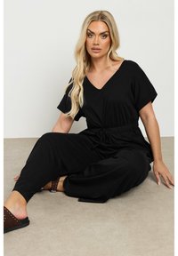 Monos de color negro hechos de una tela suave, con escote en V, mangas cortas, cintura ajustable con cordón y pantalones de corte relajado.