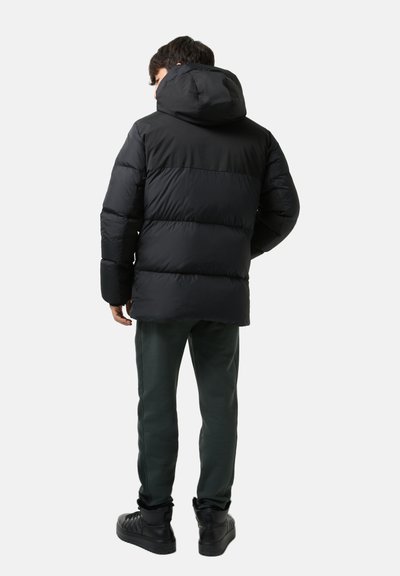 Black puffer jacket with a hood, featuring quilted sections and a smooth texture. Worn over dark green sweatpants and black boots.