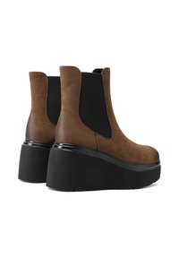 Stivali alla caviglia in suede marrone con pannelli elastici neri, punta arrotondata e suole in gomma nera spessa. Design semplice ed elegante con accenti minimi.