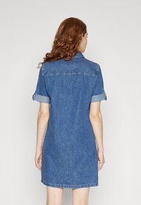 Jeansklänning med korta ärmar, knäppning vid kragen och upprullade ärmslut. Blått tyg, lätt utställd form och sömmar vid fållkant.