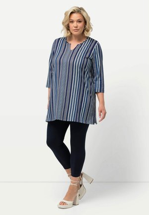 Blå og hvid mønstret tunika med V-hals, trekvartærmer og løs pasform, parret med marineblå leggings og sandaler med blokhæle.