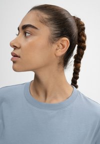 Hellblauses T-Shirt mit rundem Ausschnitt, weicher Textur und kurzen Ärmeln, getragen von einem Modell mit geflochtenem Haarschnitt, das leicht nach links schaut.