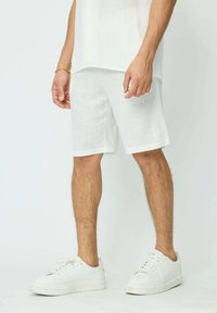 Shorts en lin blancs avec un tissu texturé et une coupe décontractée. Associés à des baskets blanches, avec une surface lisse et des lacets.
