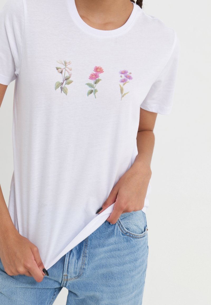 Camiseta de algodón blanca de manga corta, con diseños florales bordados en rosa, púrpura y verde en el pecho.