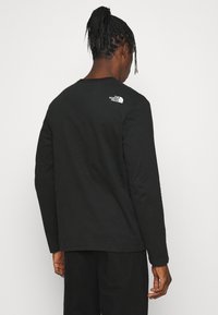 Svart långärmad t-shirt med rundad halsringning och en vit logotyp på baksidan. Tillverkad av bomull med en mjuk textur. Avslappnad passform.