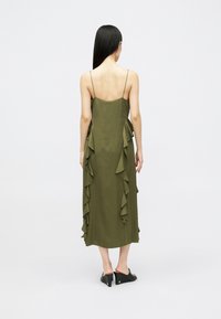 Vestido midi sem mangas verde oliva com detalhes franzidos nas laterais. Tezido suave com uma textura fluida e finas alças de espaguete.