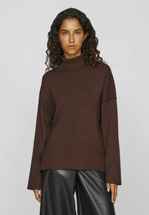 Brown turtleneck sweater with a relaxed fit, ribbed texture, and dropped shoulder seams. Paired with black leather trousers.