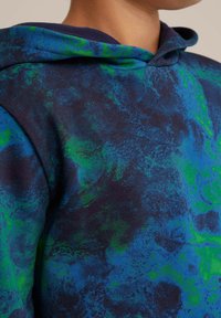 Sudadera con capucha de un patrón multicolor en azul y verde sobre una base de color navy, hecha de una tela suave con un aspecto texturizado.