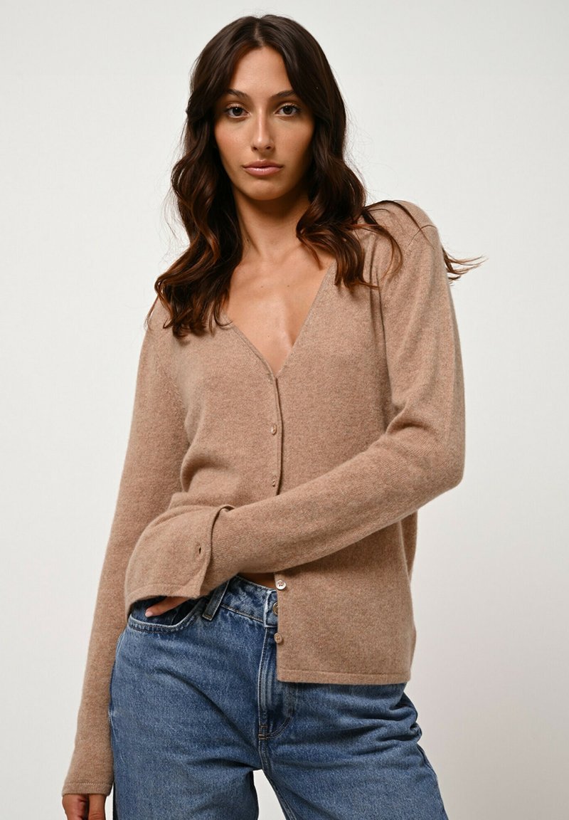 Hellbraunes Kaschmir-Cardigan mit V-Ausschnitt, Knopfleiste und langen Ärmeln. Weicher Griff und leichter Stretch, kombiniert mit blauen Denim-Jeans.