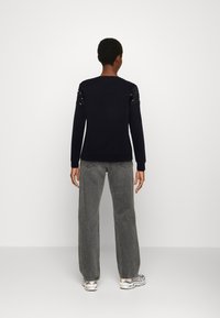 Top negro de manga larga con hombros adornados con lentejuelas, presenta un escote redondo, tejido suave y un corte relajado, combinado con unos pantalones de mezclilla gris de pierna ancha.