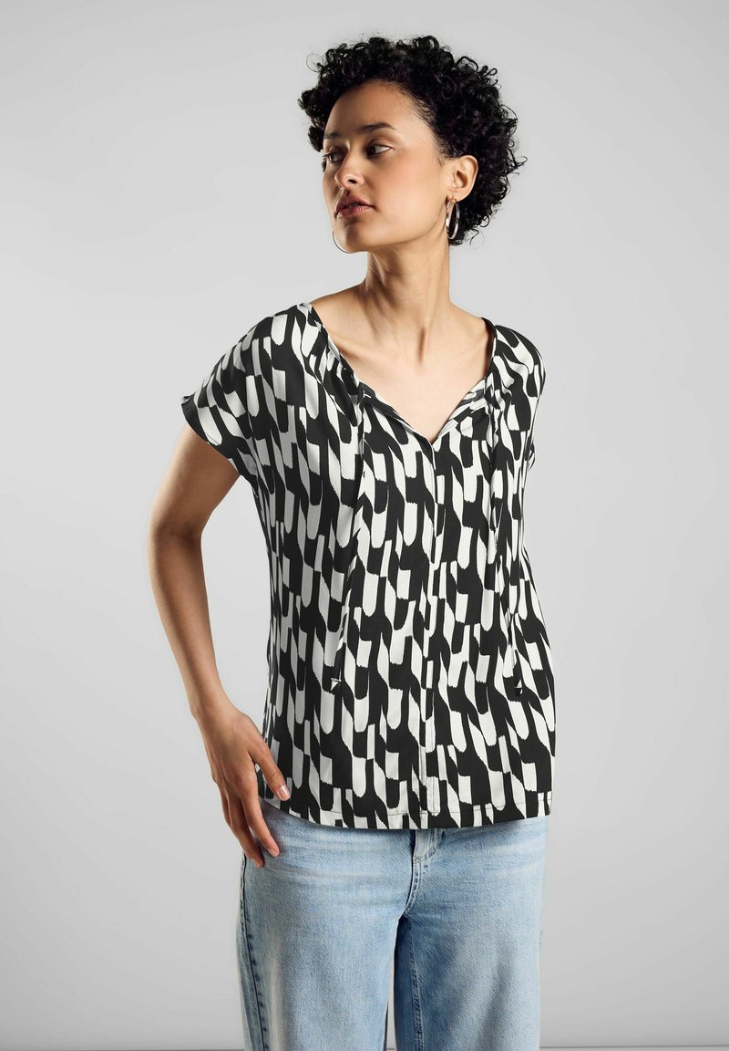 Blusa de patrón en blanco y negro con mangas cortas, escote en V y tejido suave. Combinada con vaqueros de denim azul, de corte relajado.