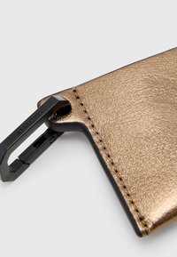 Tarjetero de cuero texturizado en oro con clip de metal negro. Presenta un acabado suave, bordes cosidos y un pequeño detalle de hardware circular.