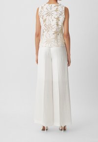 Ärmlös topp med blommig spetsdesign i beige och vitt, ihopparad med vida, flödande vita byxor. Slät, lättviktsmaterial.