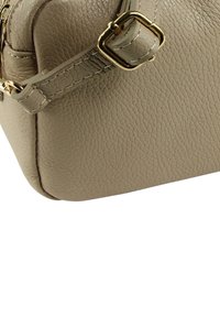 Beige leren handtas met een gestructureerde afwerking, afgezet met gouden accenten en een stevige onderkant, die de rechthoekige vorm benadrukt.