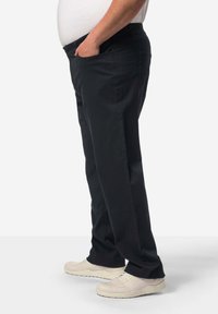 Černé kalhoty rovného střihu, vyrobené z odolné látky, s bočními kapsami a nenápadným elastickým pasem, doplněné o světlé boty.