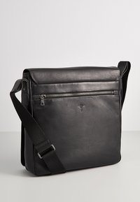 Borsa a tracolla in pelle nera con forma piatta, tracolla regolabile, tasca frontale con zip e dettaglio del logo impresso. Texture liscia.