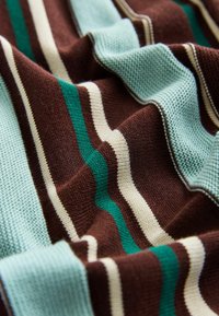 Kootud kangas, millel on vahelduvad pruunid, mündirohelised, kreemjad ja roheka tooniga triibud, tekstuurse viimistlusega ja nähtavate ahelatega.