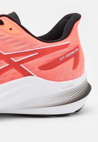 Talons de chaussure de course corail vif avec logo rouge, semelle blanche portant l'inscription PureGEL et marquage GT-2000 12 sur tissu en mesh.