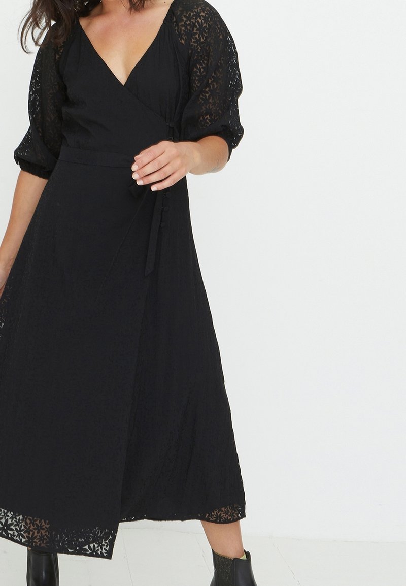 Zwarte wikkeljurk met bloemenkant mouwen en accenten, met een V-hals, tailleband en een flowy, midi-lengte rok. Geweven stof.