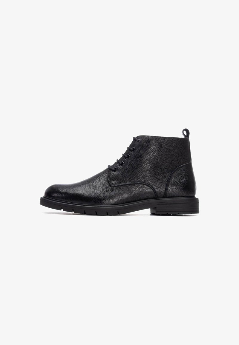 Botas de tobillo de cuero negro con superficie texturizada, seis ojetes y suela de goma. Presenta un lazo en la parte posterior para facilitar el calzado.