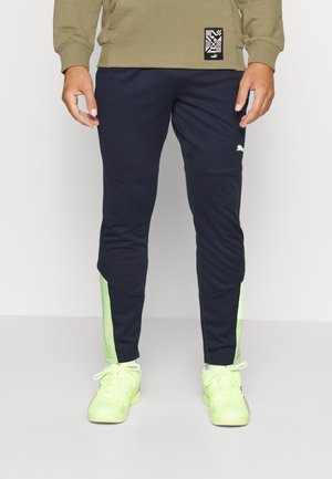 Pantalones deportivos navy con acentos verdes, con un diseño ajustado, cintura elástica y un logotipo en el muslo. Hechos de tela ligera.