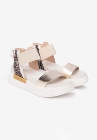 Sandales de sport beige et doré métallique avec des accents de motif léopard, semelle blanche épaisse et larges sangles élastiques pour un maintien sécurisé.